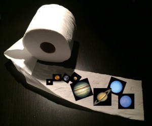 Miniature images of the planets of the solar system are arranged across a length of toilet paper.