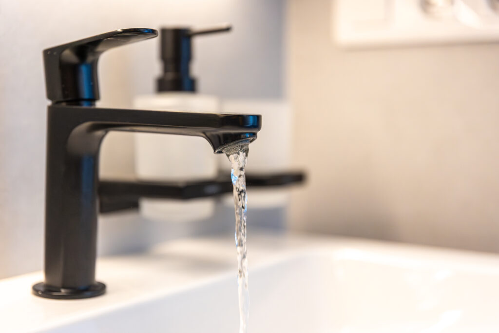 Black bathroom faucet with a steady stream of clear water flowing into a white sink, representing reliable access to clean water.